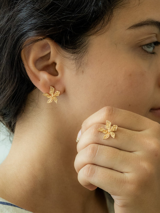 Close-up of a person wearing gold flower earrings and a ring.