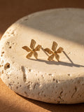Gold flower-shaped earrings on a textured stone surface