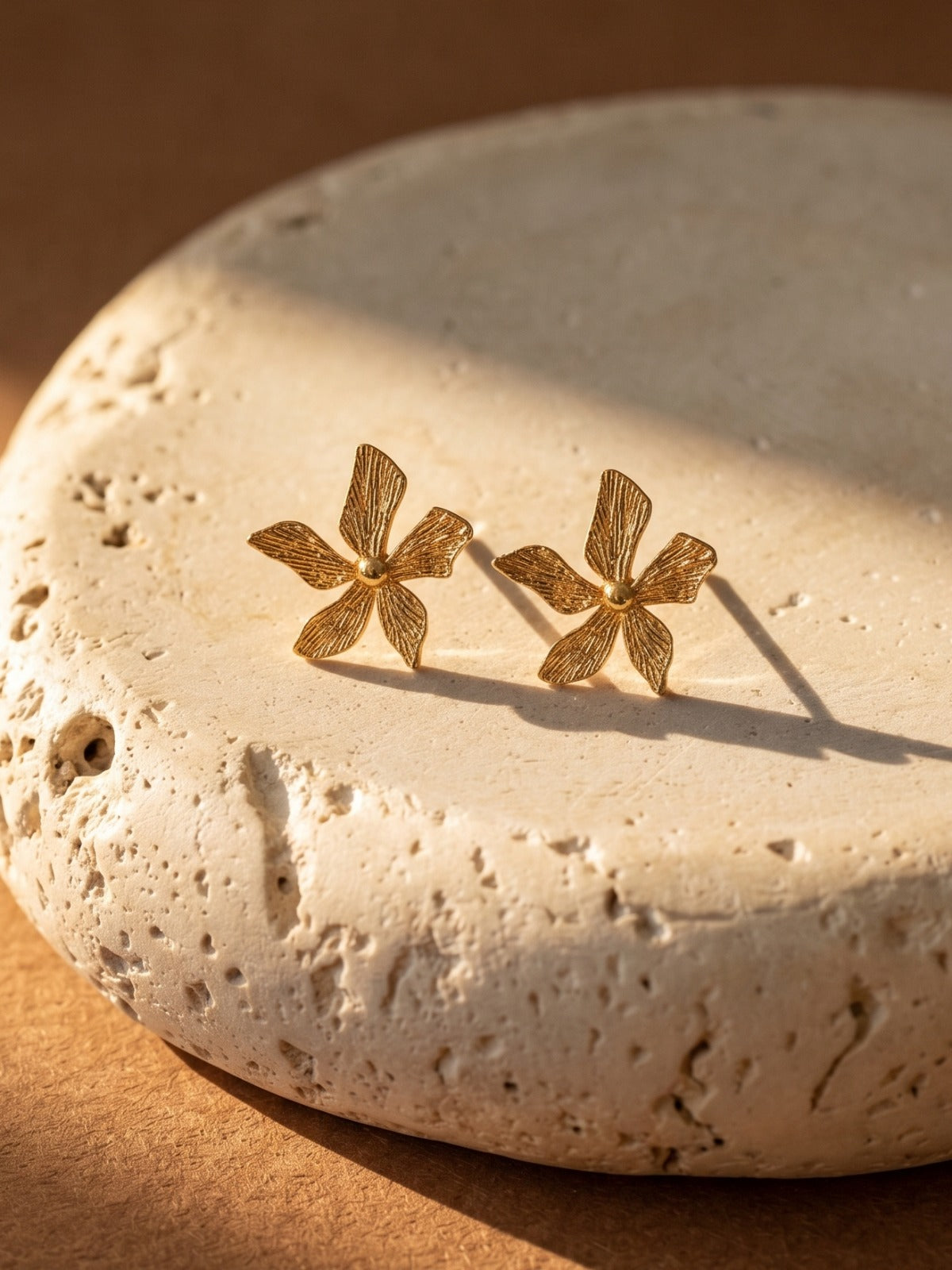 Gold flower-shaped earrings on a textured stone surface