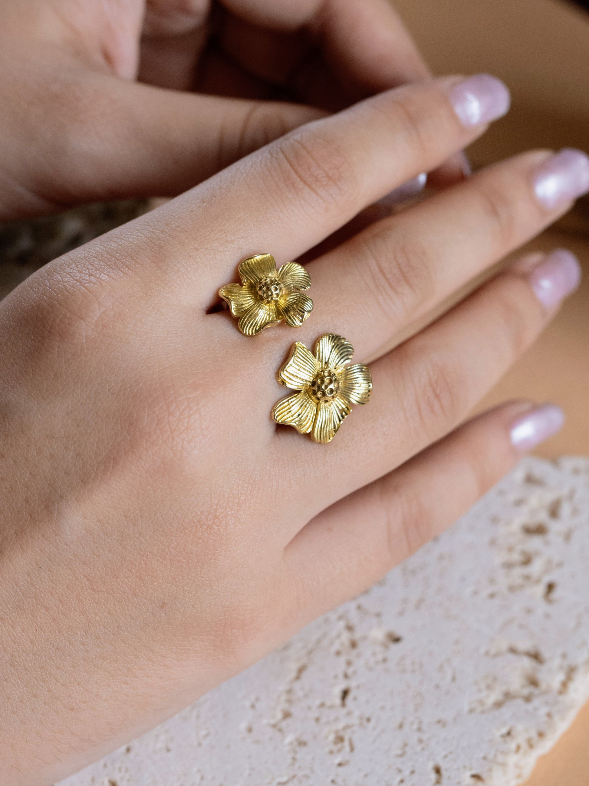 Gold flower-shaped earrings on a hand with a blurred background
