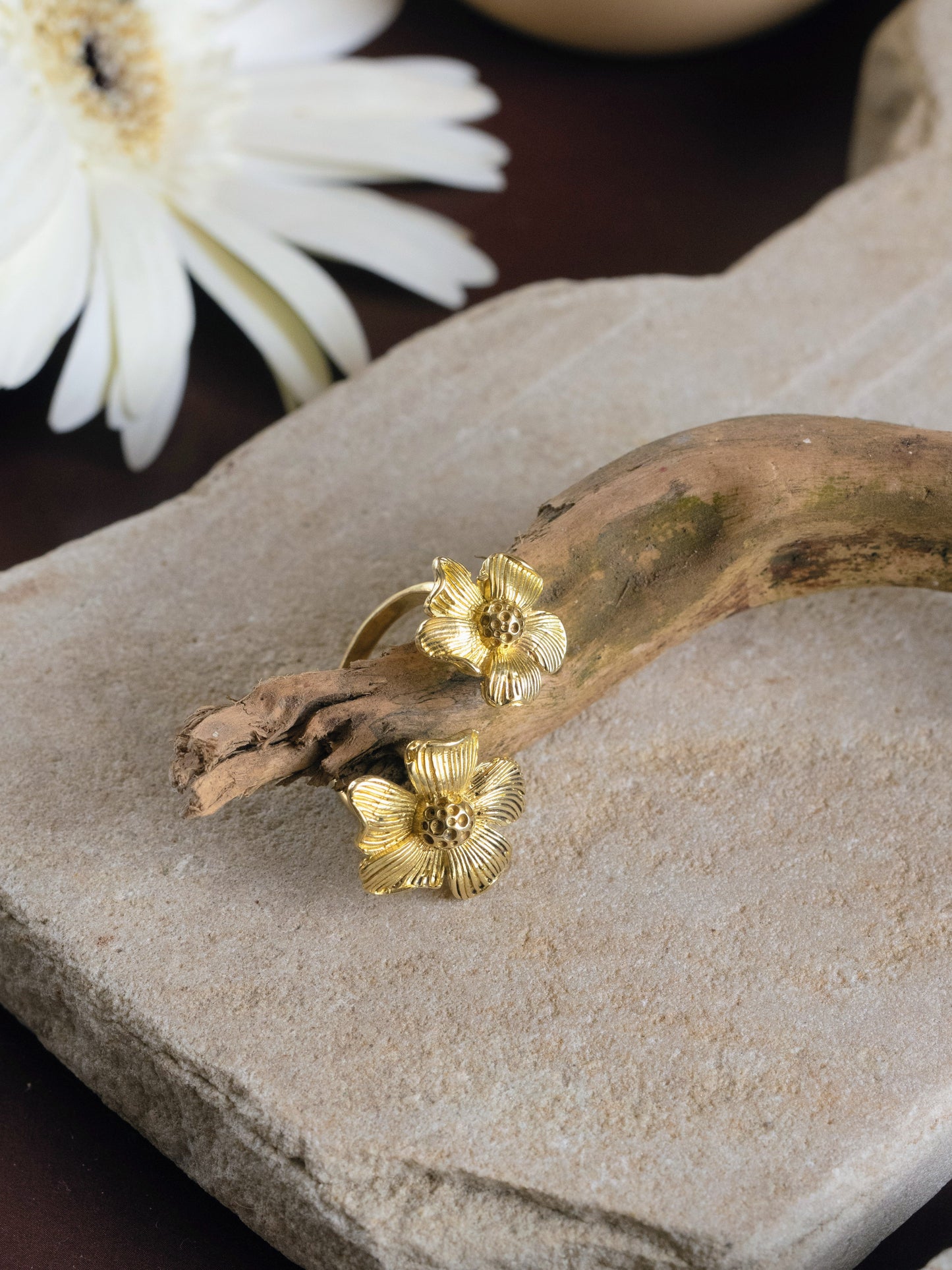 Gold floral bracelet on a stone surface with a white flower in the background